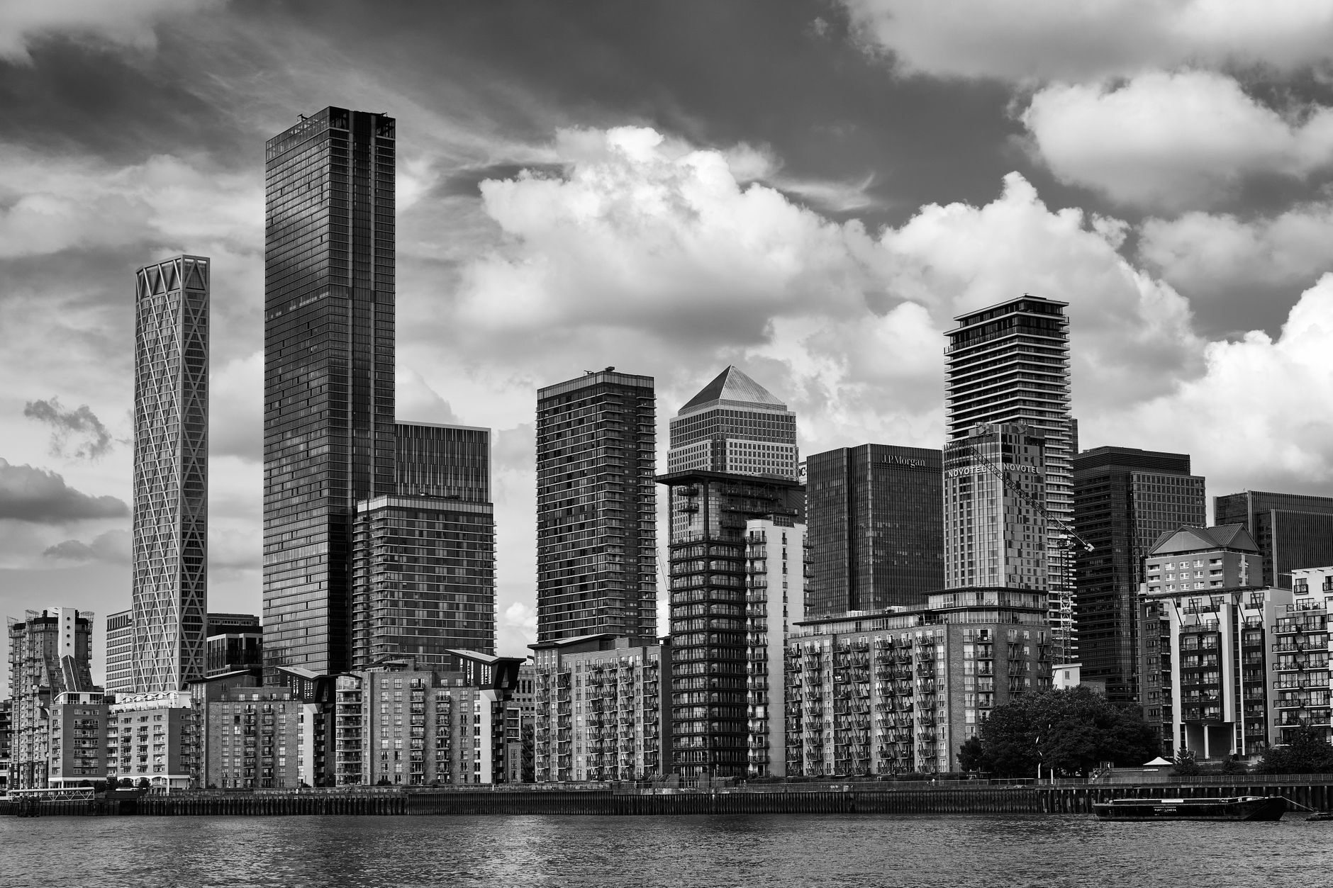Black and white cityscape of London's iconic Canary Wharf under a cloudy sky.