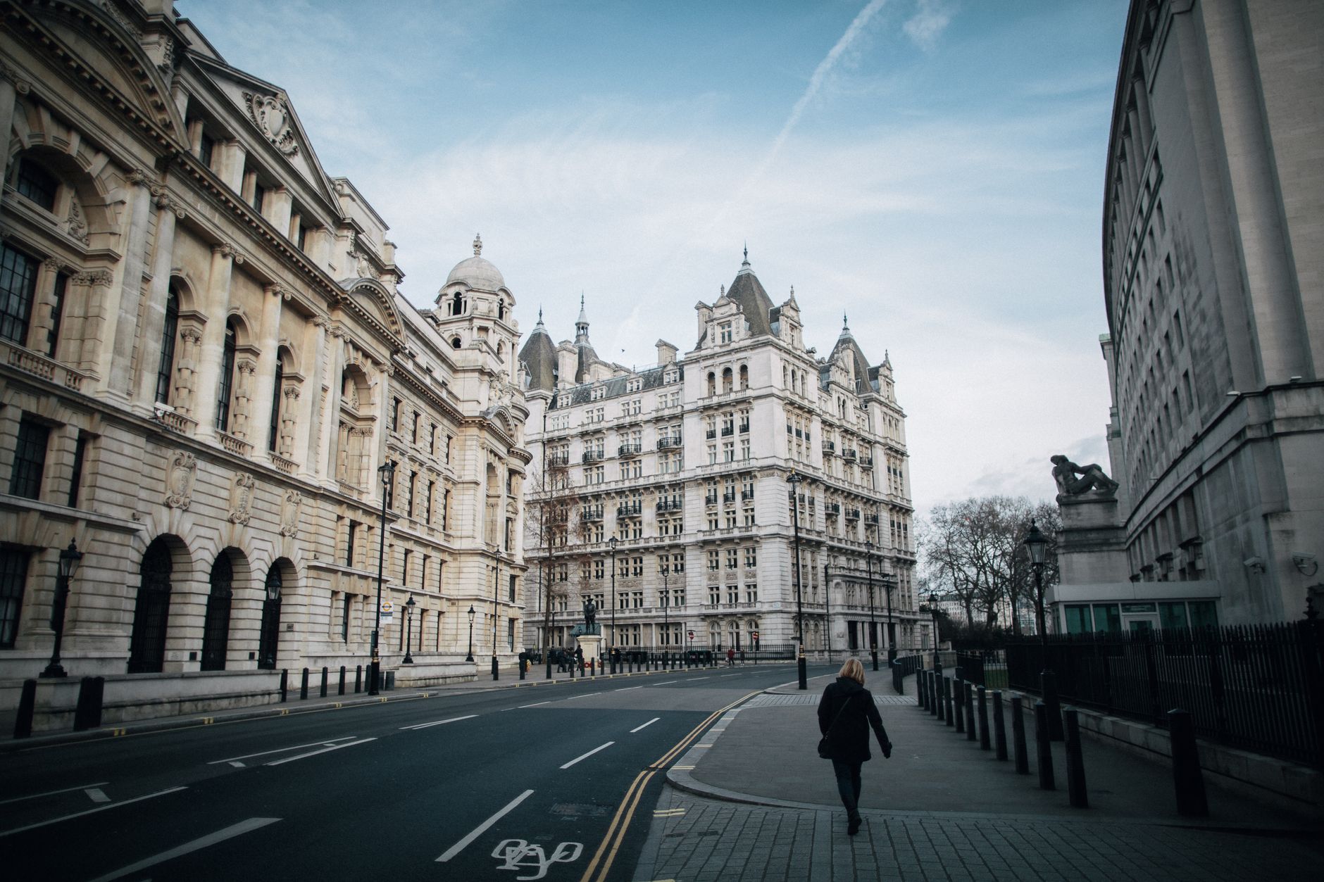 Back view of anonymous female strolling on walkway between road and aged masonry building exteriors in Whitehall London